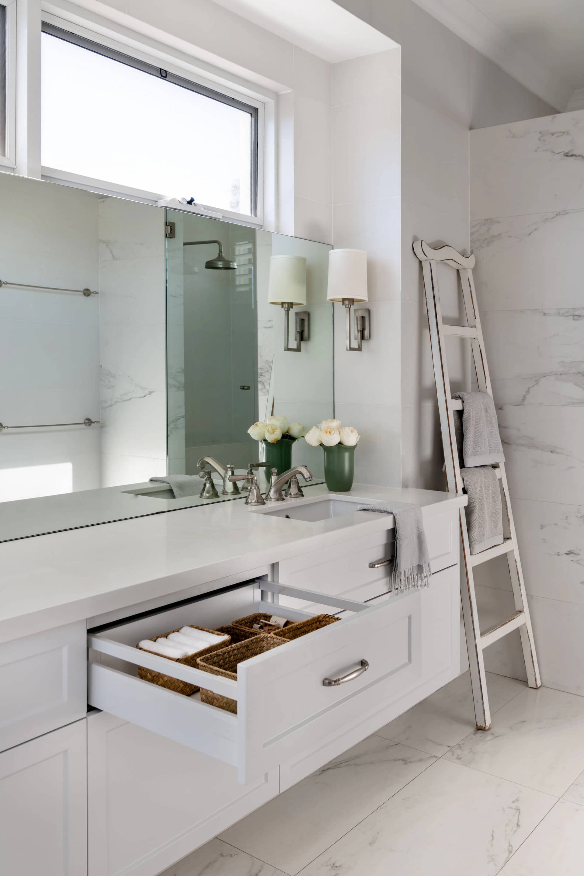 A white bathroom vanity with an open drawer and a leaning ladder