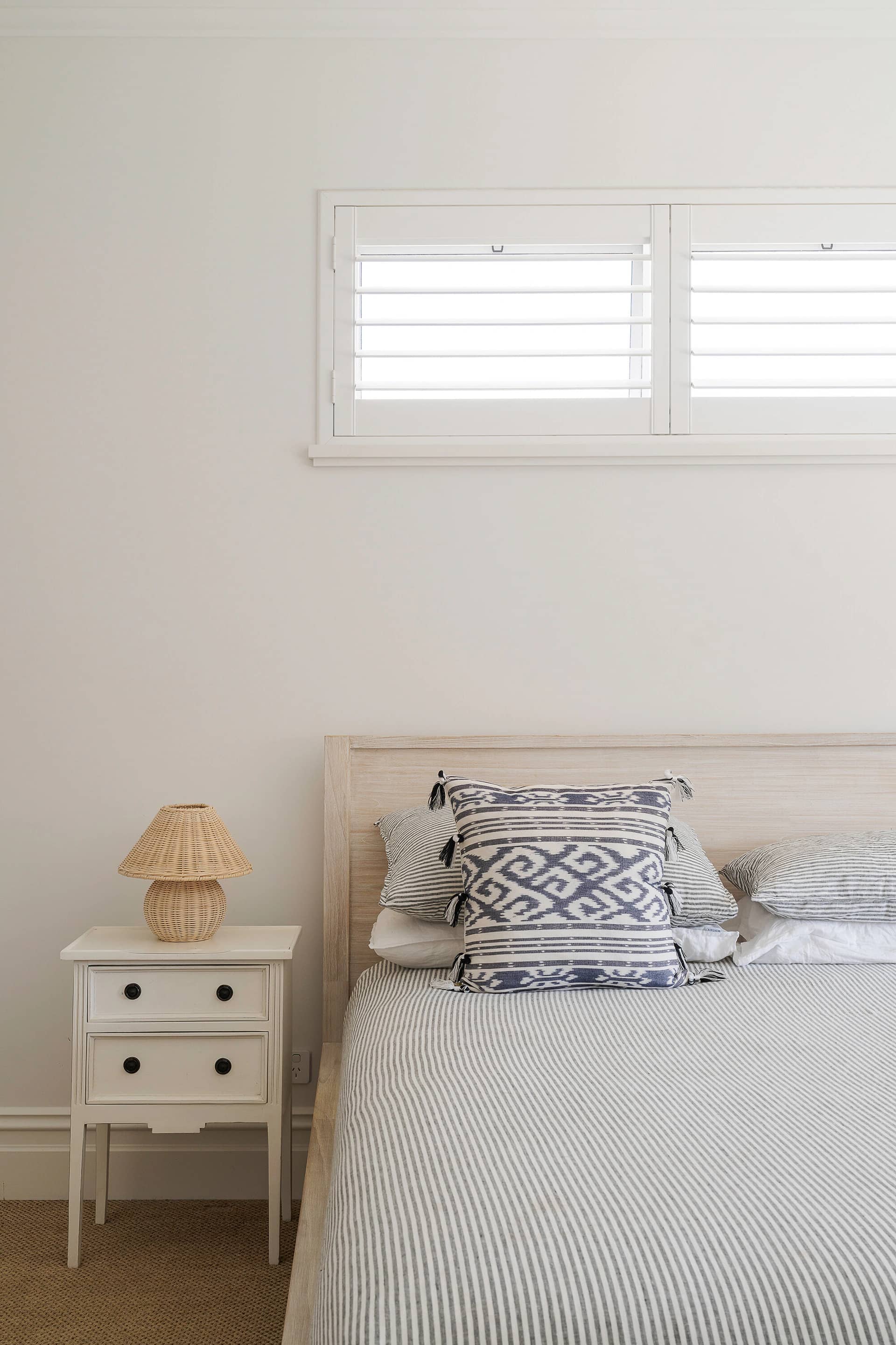 A calm styled bedroom with a linen bedhead, white side table and soft light