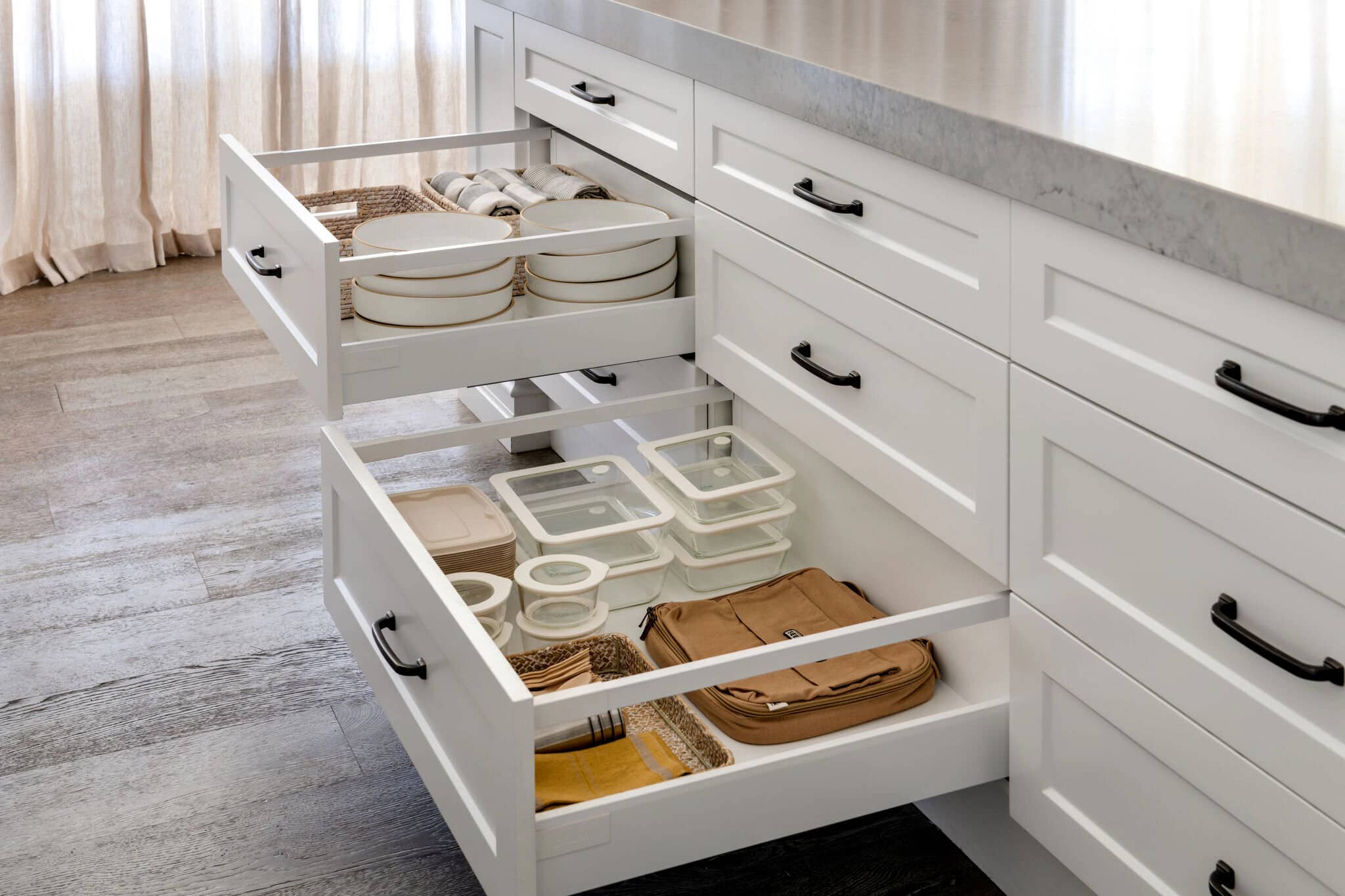 Open kitchen drawers holding plates and clear containers