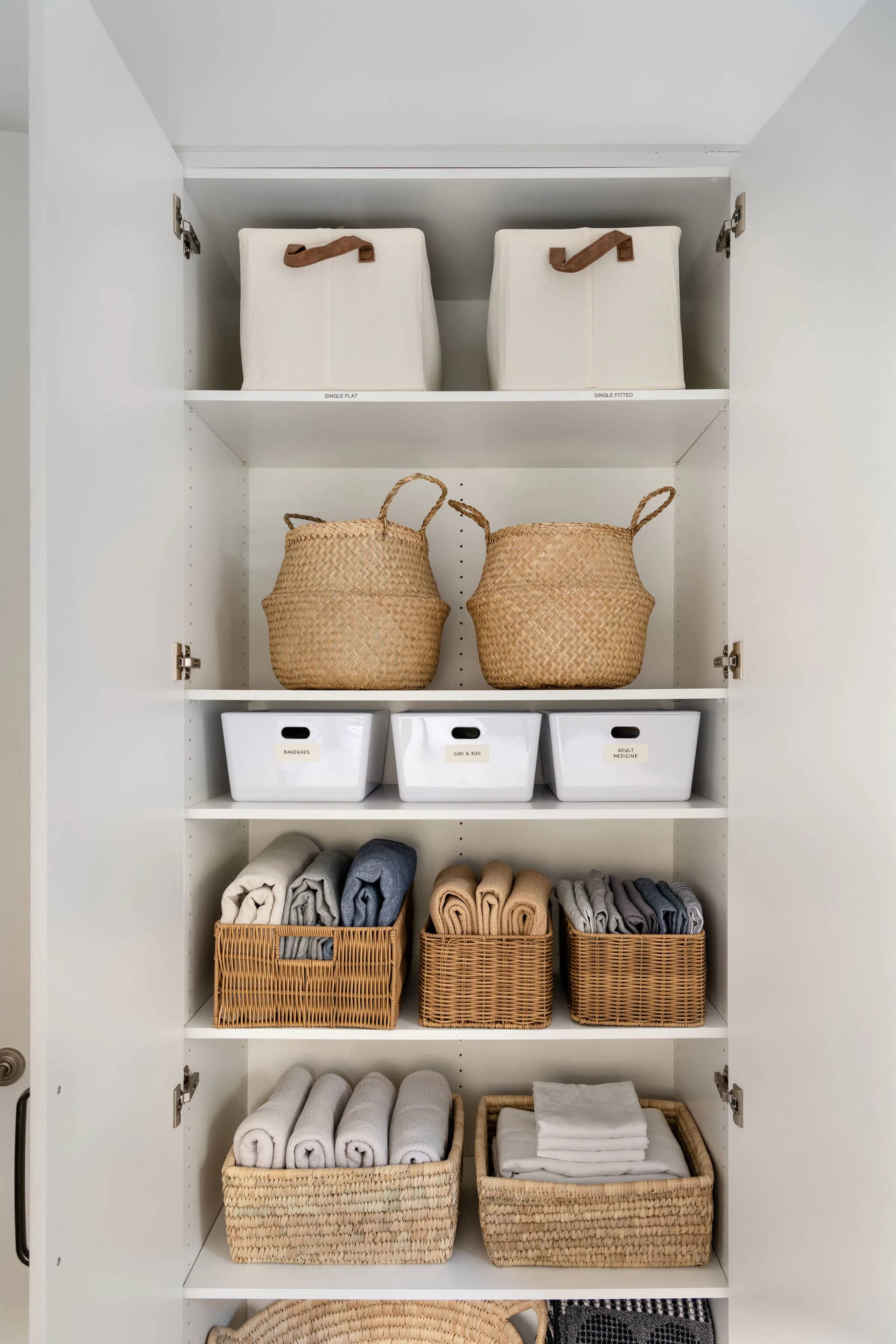 A linen cupboard with folded towels and woven baskets