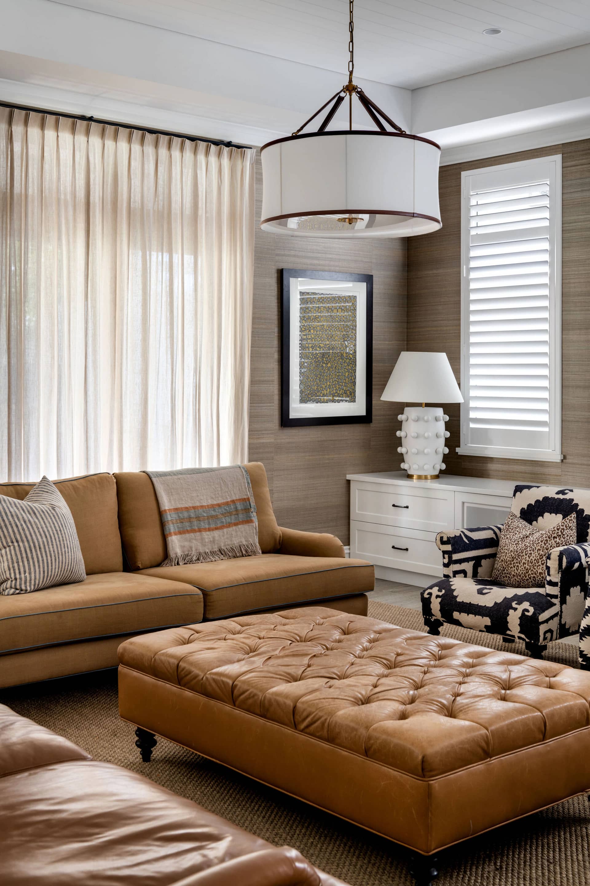 A living room with a tan leather sofa, tufted ottoman and layered lamps