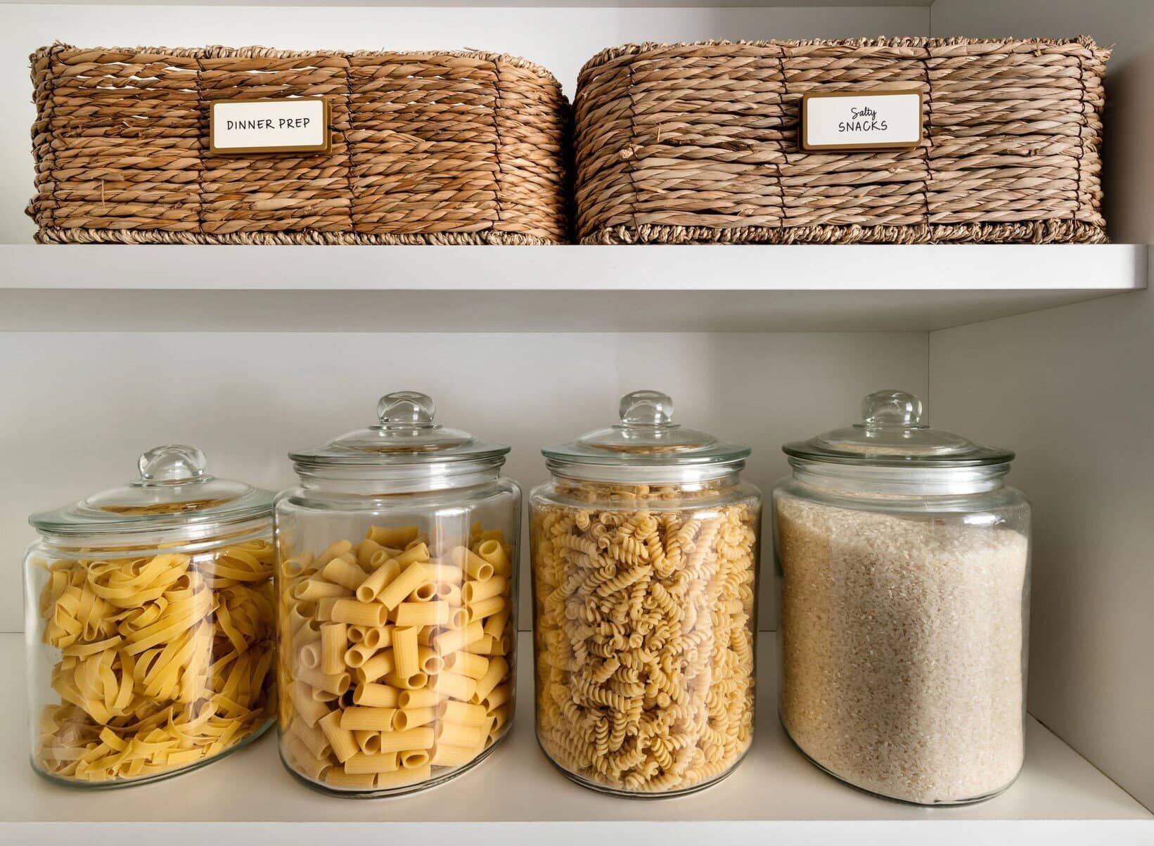 Glass jars of pasta and rice under a shelf of labelled baskets