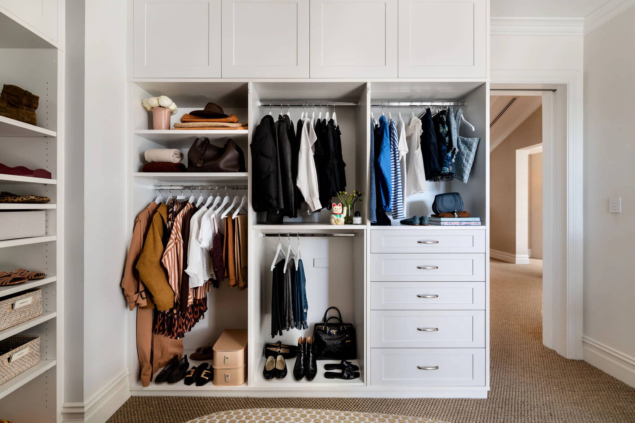 A wide wardrobe with hanging clothes, shoes and folded pieces on open shelves